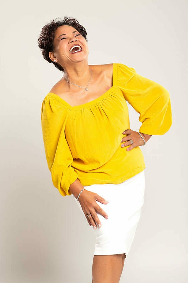 Full body image of Michelle Mras laughing in a white skirt and yellow top.