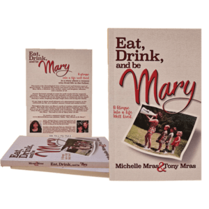 A grouping of the book Eat Drink and Be Mary. The Cover contains what appears to be mom and 4 kids marching. The title and author credit to Michelle and Tony Mras